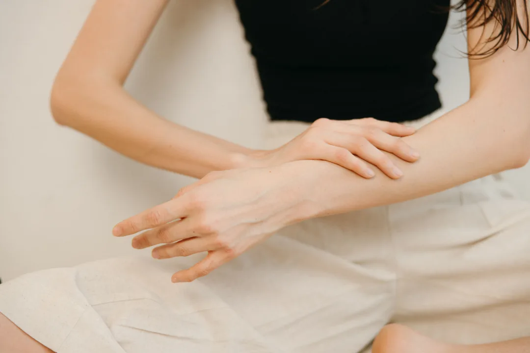 Hands spreading body lotion over dry forearm skin in daylight